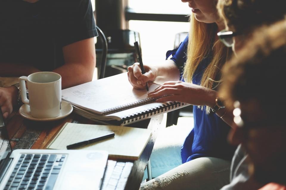 Personas trabajando alrededor de una mesa con portatiles y cuadernos