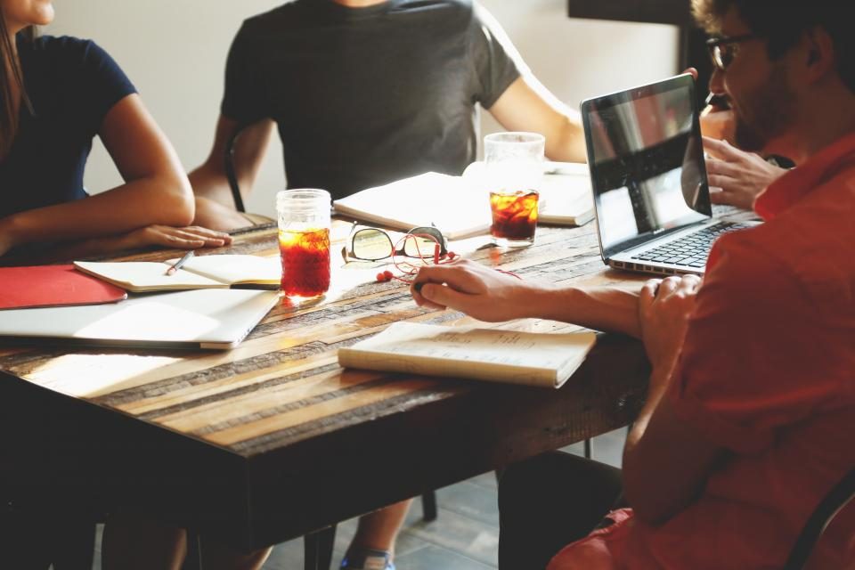 Grupo de personas trabajando en una mesa con portatiles y cuadernos