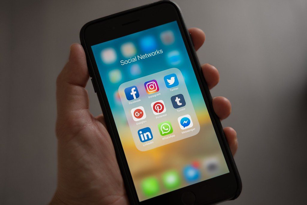Mano sosteniendo un movil con una carpeta de aplicaciones sociales que incluye Instagram, Facebook y WhatsApp
