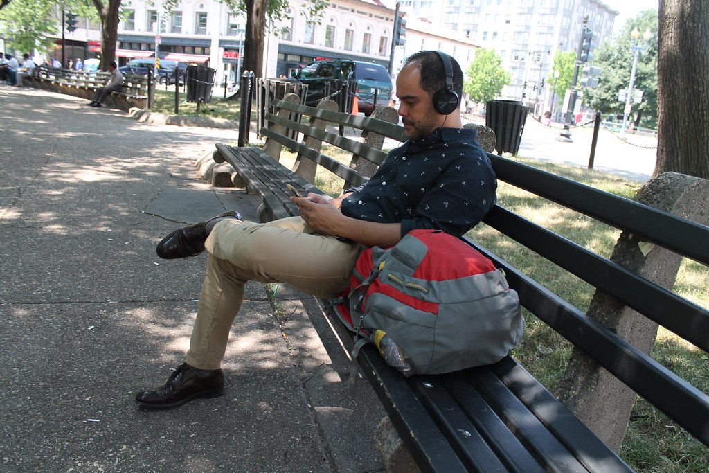 Hombre sentado en un banco de un parque consultando el movil con auriculares puestos